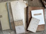 Plusieurs vieux livres sont posés sur une table en bois, à côté d'un stylo et d'une feuille de papier.