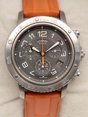 un bracelet orange autour d'un cadran de montre posé sur une surface blanche