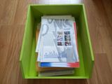 une boîte verte remplie de magazines et de journaux posée sur un plancher en bois
