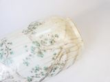 un vase blanc orné de fleurs vertes, posé sur une table