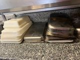 several trays of food sitting on top of a counter under a metal shelf