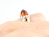 a woman ' s hand holding a ring with an orange stone on it