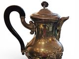 une cafetière en argent avec une poignée noire, posée sur un socle
