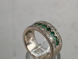 a close up of a diamond and emerald ring on a clear surface