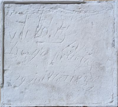 une vieille plaque en pierre portant une inscription, devant un mur de briques