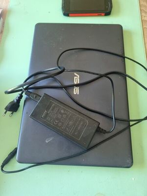 un ordinateur portable posé sur une table, avec son chargeur branché