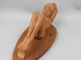 sculpture en bois représentant un homme assis sur une planche de surf, posée sur une surface blanche