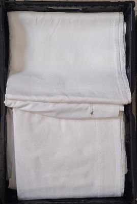 une valise noire remplie de linge de maison blanc, posée par terre