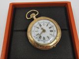 une montre de poche en or dans un écrin, posée sur une surface blanche