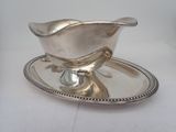 a silver sauce boat on a silver plate on a white table