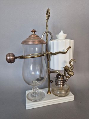 une cafetière en verre avec une poignée en laiton posée sur un socle en marbre