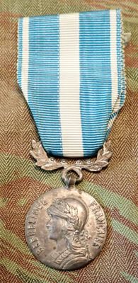 an old silver medal with a blue and white ribbon and a silver medal