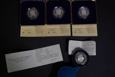 Trois pièces d'argent sont posées sur une table, à côté d'une paire de ciseaux.