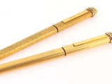 two gold colored pens sitting next to each other on a white surface