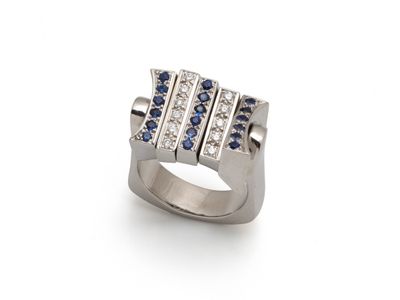 un gros plan d'une bague posée sur une surface blanche, ornée de pierres bleues et blanches