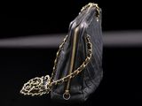 black leather purse with gold chain on black background