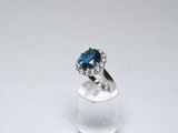 une photo d'une bague en diamant bleue et blanche posée sur une surface transparente