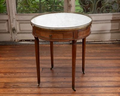une petite table ronde avec un plateau en marbre posée sur un parquet