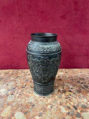 black vase sitting on top of a table with a red wall in the background