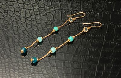 une paire de boucles d'oreilles en perles d'or et de turquoise sur fond noir