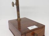 un microscope à l'ancienne posé sur une boîte en bois, sur fond blanc