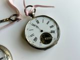 a silver pocket watch with roman numerals and a pink ribbon