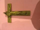une croix dorée sur un mur rose, avec l'ombre d'une personne