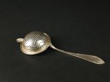 a silver tea strainer on a black surface
