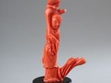 une sculpture orange représentant une femme tenant un pot, posée sur un socle noir