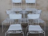 four white metal chairs with white cushions sit in front of a wall