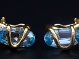 paire de boucles d'oreilles dorées ornées de cristaux de topaze bleue sur fond noir