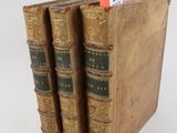 trois vieux livres sont empilés sur une surface blanche