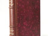 an old book with a red cover sitting on top of a white surface