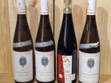 four bottles of wine are lined up on a wooden shelf