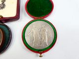 a silver medal in a red case next to a green box