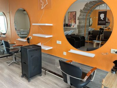 une photo d'un salon de coiffure avec des fauteuils et des miroirs