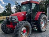 une photo d'un tracteur rouge garé sur un terrain en gravier