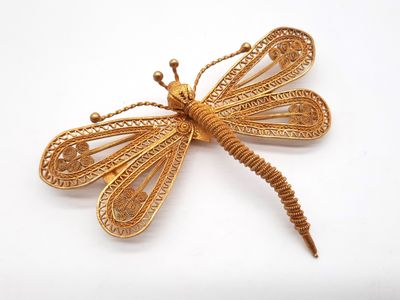 une image représentant une broche en forme de libellule dorée sur fond blanc