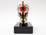 a white and gold mask on a black stand