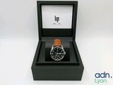 une photo d'une montre dans un coffret noir, avec un bracelet marron