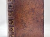 an old brown book sitting on top of a table next to a glass of wine