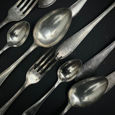 de nombreuses cuillères et fourchettes en argent posées sur une table noire