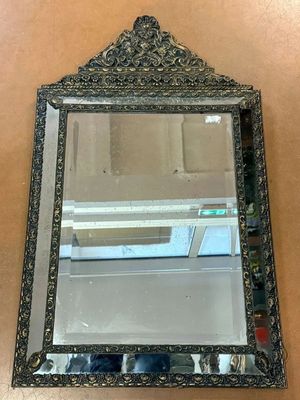 an ornate mirror on a wall with a shelf in the background
