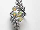 un gros plan d'une bague posée sur une surface blanche, entourée de fleurs et de feuilles