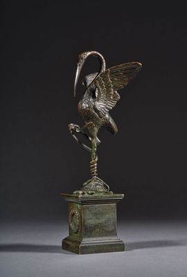 statue en bronze représentant un oiseau sur un socle, avec une horloge en arrière-plan