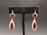 une paire de boucles d'oreilles en rubis et or, posée sur un socle noir