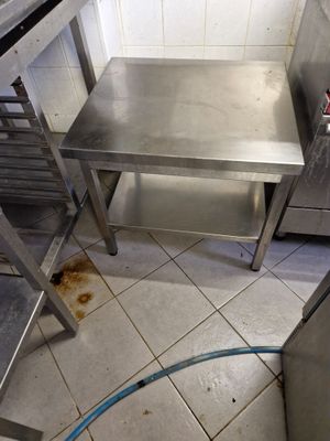 une table en acier inoxydable dans une cuisine, avec un tuyau d'arrosage posé par terre