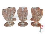four glass goblets are lined up in a row on a white surface