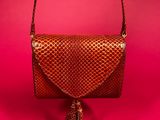 a brown purse with a tassel on a pink background