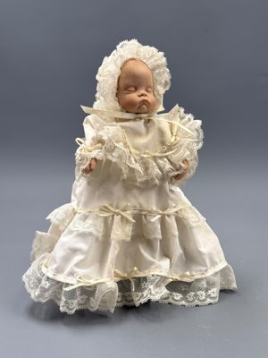 une poupée ancienne en porcelaine représentant un bébé vêtu d'une robe blanche et d'un bonnet